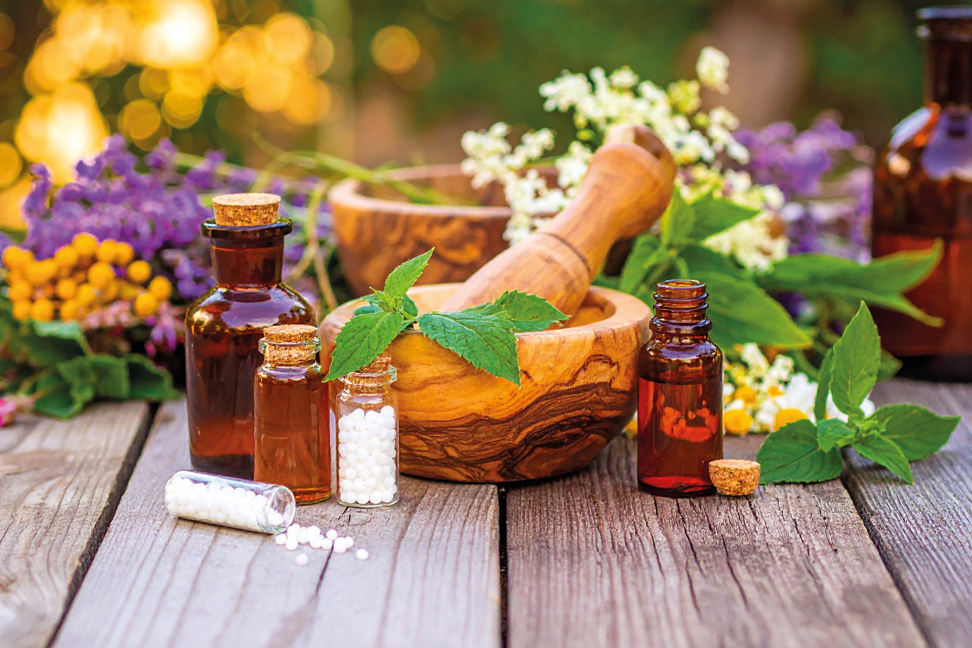 Naturheilmittel mit frischen Kräutern, homöopathischen Globuli, ätherischen Ölen und Mörser auf einem Holztisch